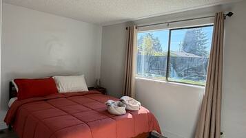 A bedroom with a bed, a window with curtains, and a ceiling light.