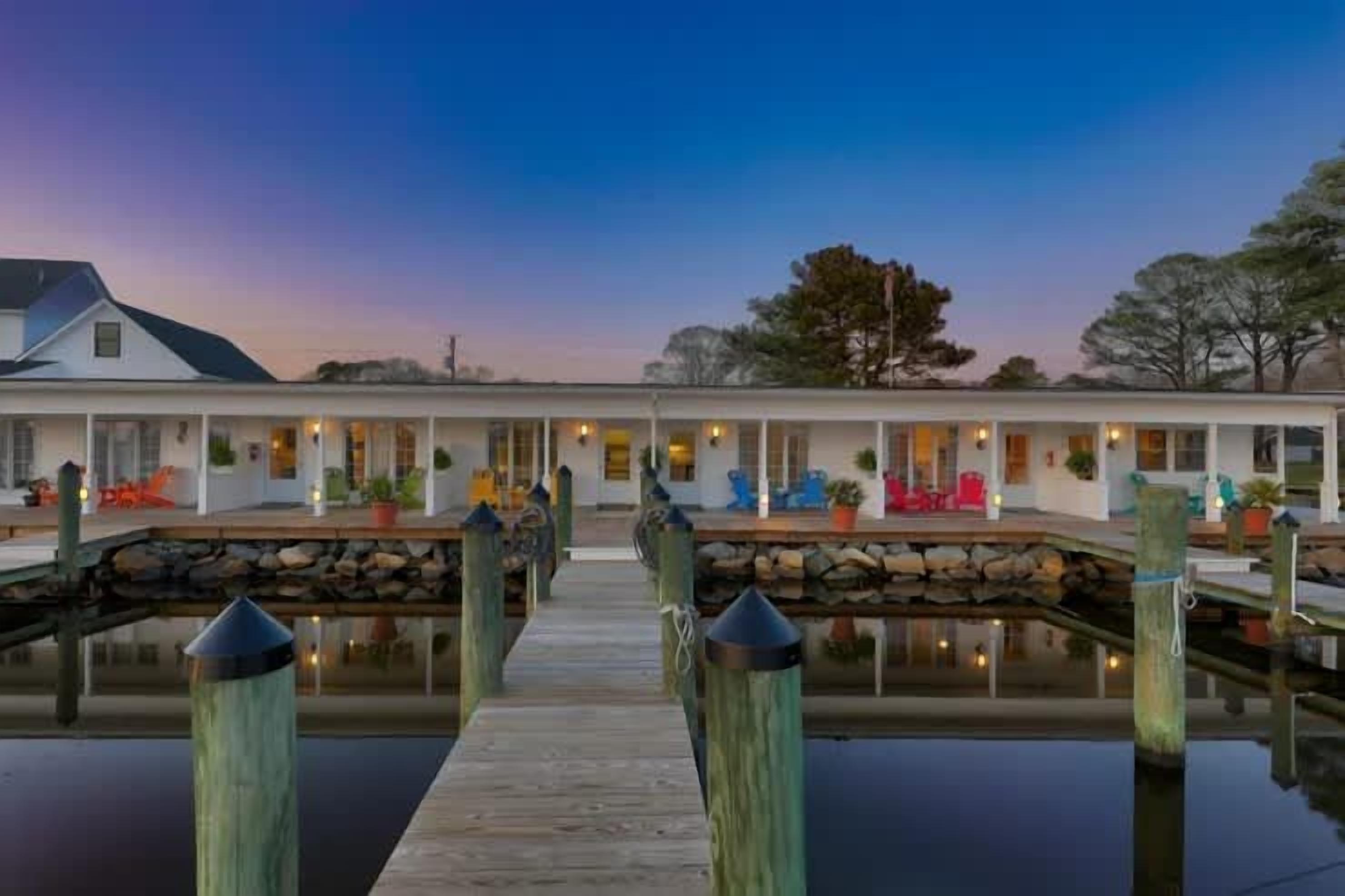 A waterfront property with a dock leading to a house with multiple windows and outdoor seating.