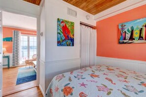 A bedroom with a bed, a painting of a parrot, and a view of the sea through a window.
