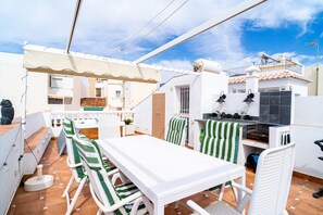 Eine Terrasse im Freien mit Esstisch und Stühlen, einem Grill und Blick auf die umliegenden Gebäude.