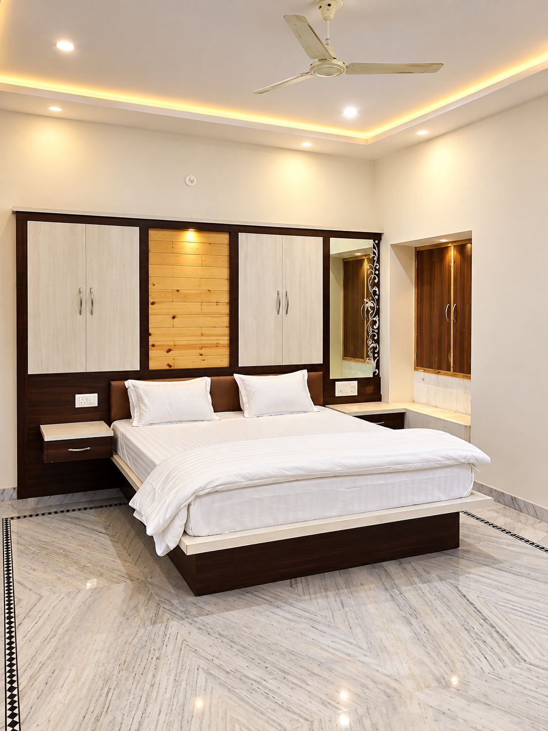 A bedroom with a bed, wooden wardrobe, a mirror, and a ceiling fan.