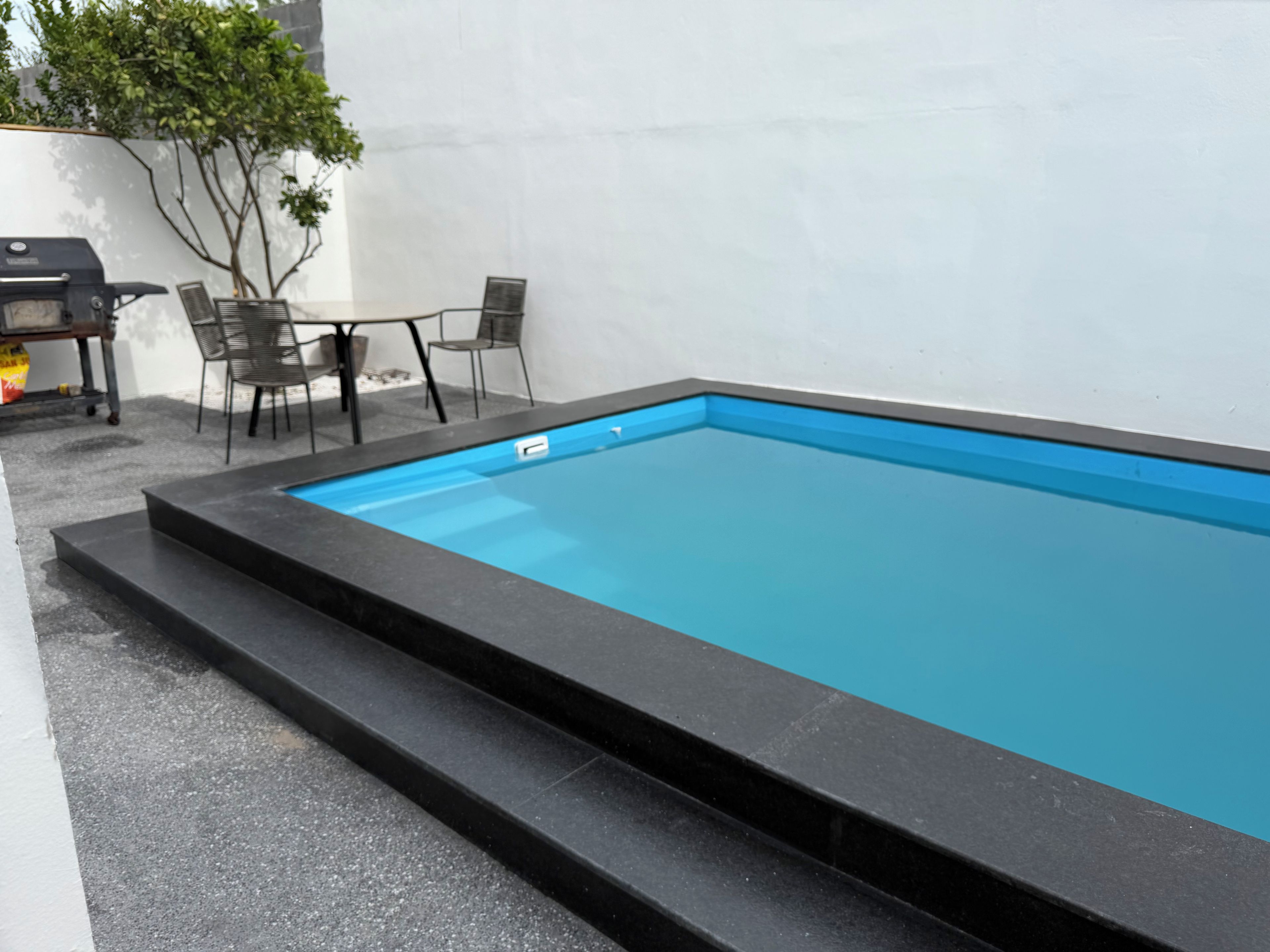 Una piscina rectangular con borde negro, rodeada por un suelo de hormigón y una pared blanca.