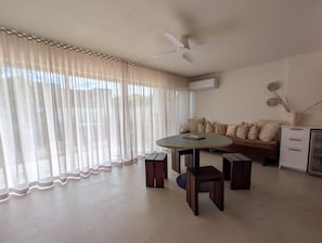 Una sala de estar con una mesa redonda, dos sillas, un sofá, un ventilador de techo y un armario blanco.