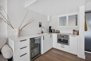 A modern kitchen with white cabinetry, a built-in oven, and a coffee maker. - Contemporary 1B Apt - 900m to Hastings St (Noosa Heads)