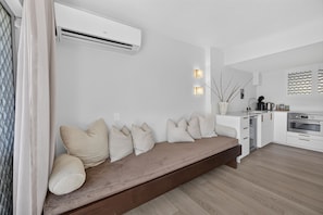 A modern living room with a built-in bench, a kitchen area, and an air conditioning unit. - Contemporary 1B Apt - 900m to Hastings St (Noosa Heads)