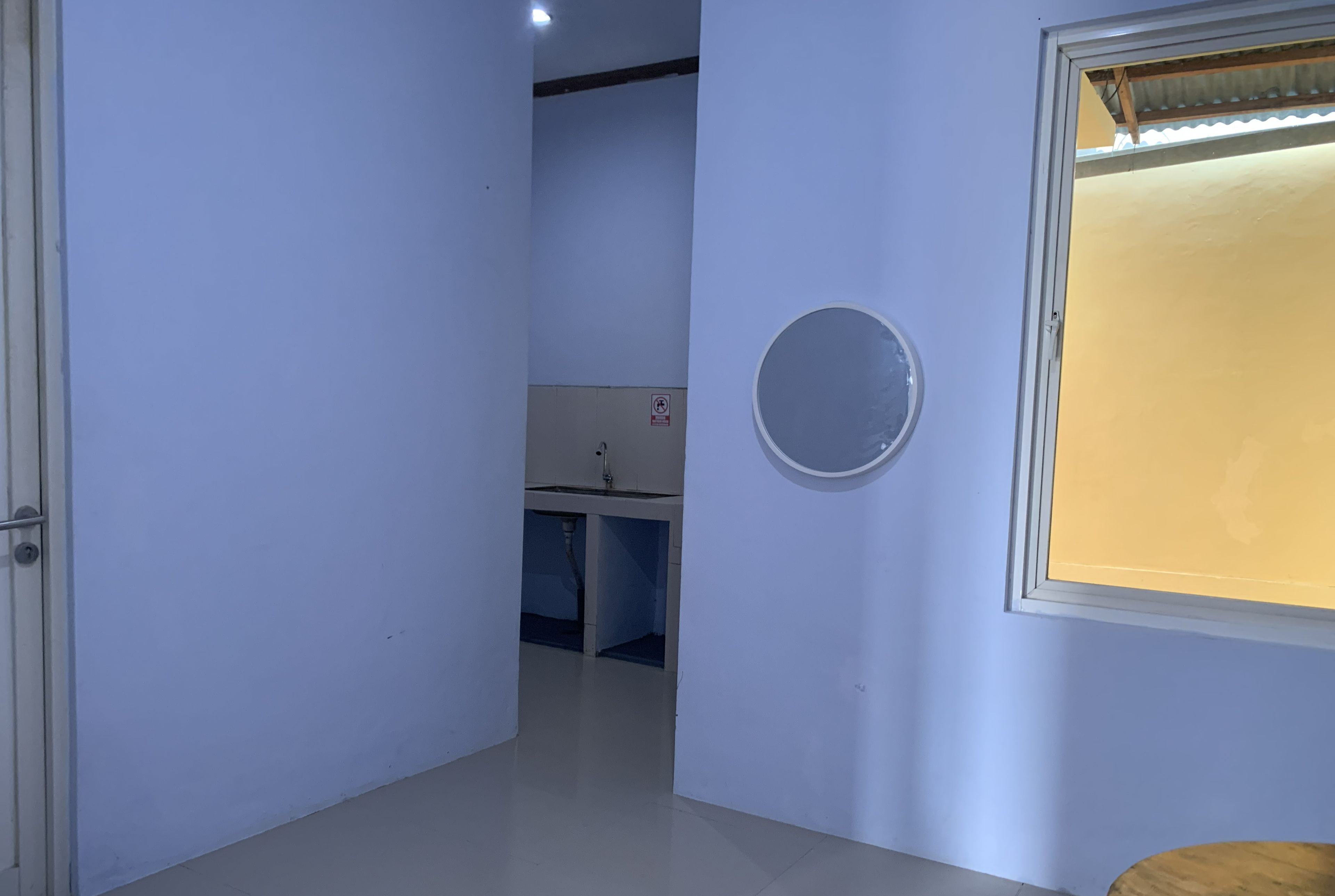 Ein schmaler Flur mit einer Tür links, einem Fenster rechts und einem Waschbecken im Hintergrund.