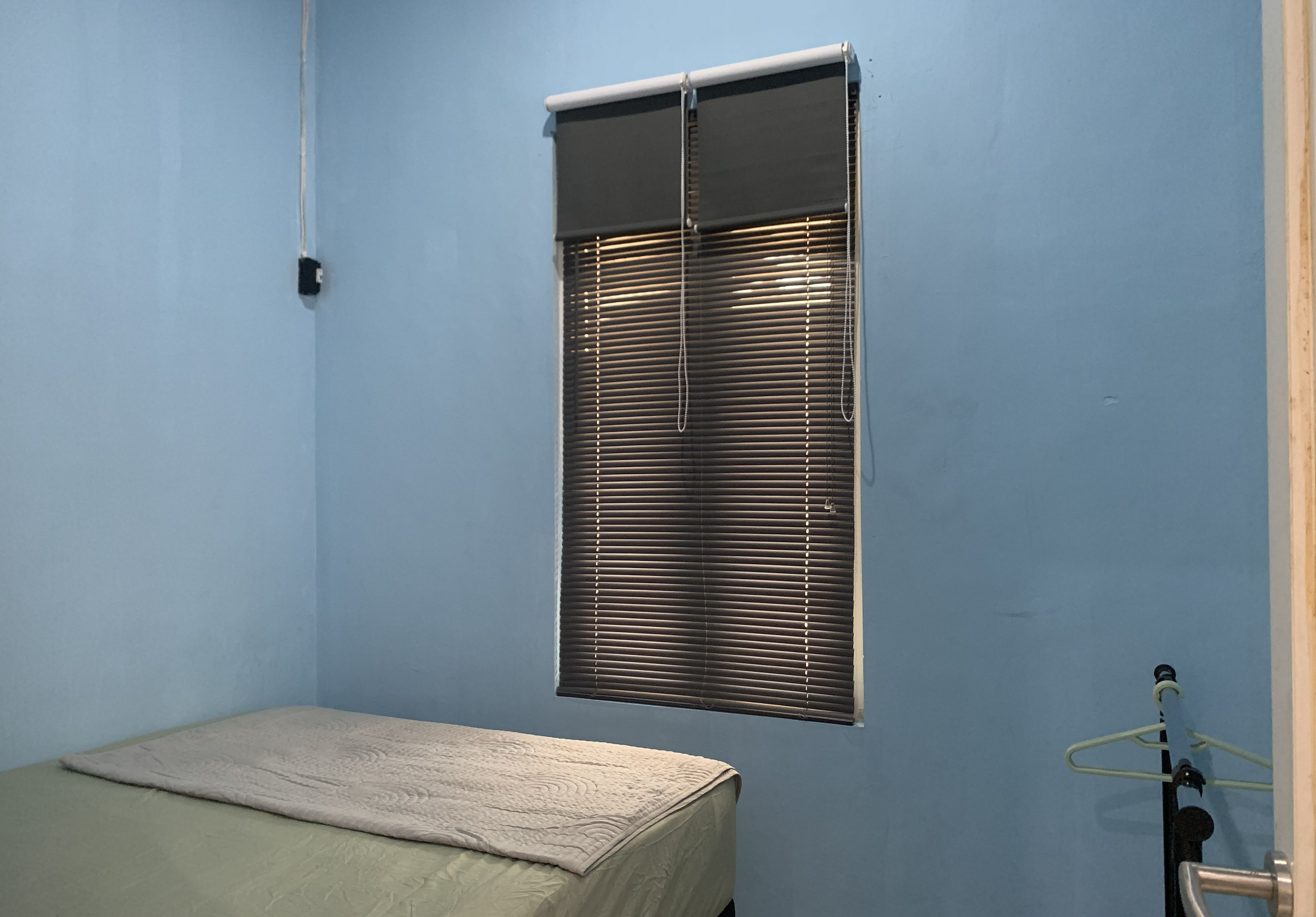 Ein Zimmer mit einem Bett, einem Fenster mit Jalousien und einer Tür mit Handtuchhalter.