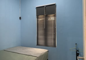 Ein Zimmer mit einem Bett, einem Fenster mit Jalousien und einer Tür mit Handtuchhalter.
