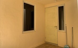 Ein Zimmer mit geschlossener Tür, einem Fenster und einem an der Wand angelehnten Besen.