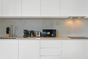Eine moderne Küche mit weißen Schränken, einer Edelstahlspüle, einer Kaffeemaschine, einem Toaster und einer Mikrowelle.