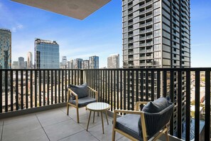 Ein Balkon mit zwei Stühlen und einem kleinen Tisch, mit Blick auf eine Skyline moderner Gebäude.
