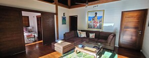 A living room with a brown sofa, a coffee table, and a painting on the wall. - Moorea Villa with Hot Tub & Outdoor Bath – Walk to Pool, Tennis & Gym (Moorea-Maiao)