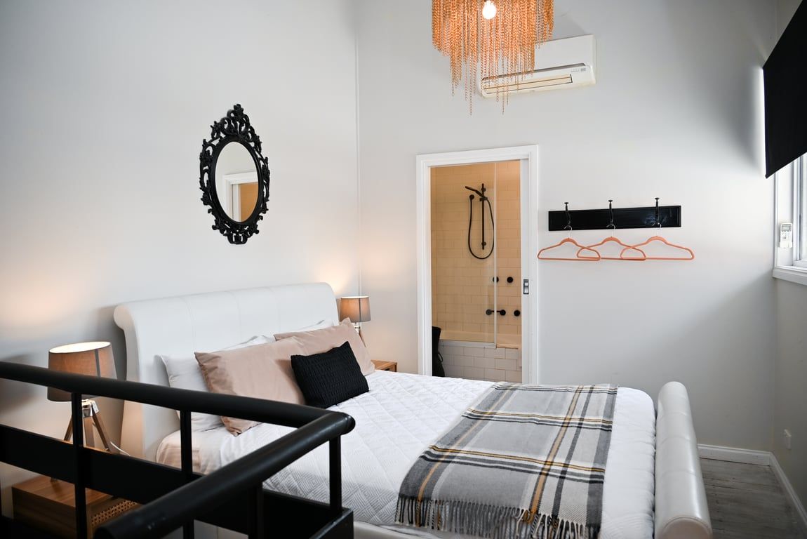 A modern bedroom with a bed, bedside lamps, a mirror, a shower, and a coat rack.