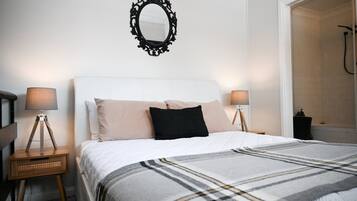 A bedroom with a bed, two bedside tables with lamps, a mirror on the wall, and a shower area.