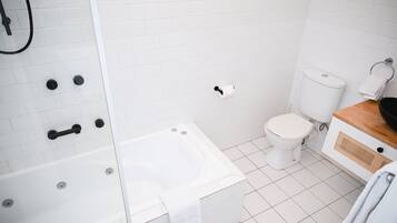 A bathroom with a white bathtub, toilet, and a shower area.