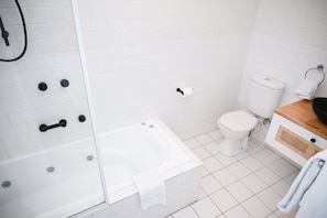 Un baño con una bañera blanca, inodoro y zona de ducha.