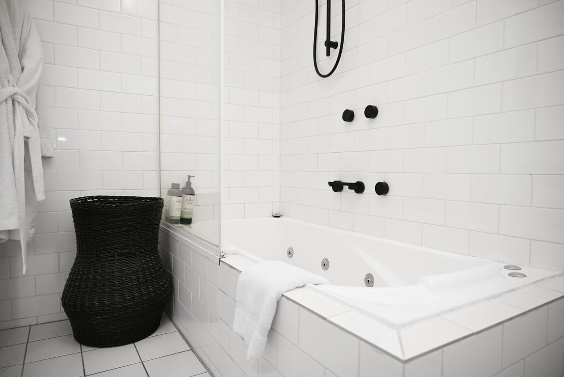 Une salle de bain moderne avec une baignoire blanche, un panier en osier noir et une serviette blanche posée sur le sol.