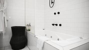Un bagno moderno con una vasca da bagno bianca, un cesto in vimini nero e un asciugamano bianco sul pavimento.