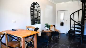 A dining area with a wooden table and chairs, a black spiral staircase, and a black-framed window.