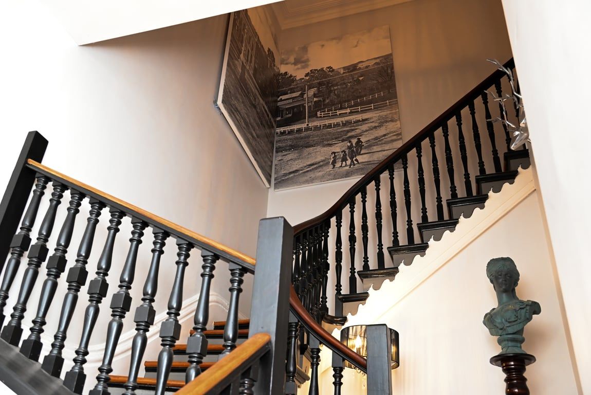 A staircase with black balusters and wooden steps, leading to a landing with a black and white photograph on the wall.