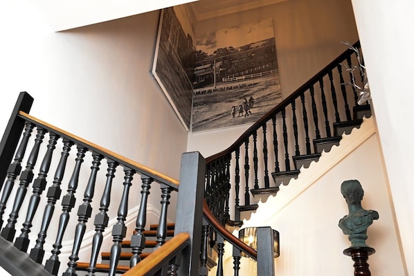 A staircase with black balusters and wooden steps, leading to a landing with a black and white photograph on the wall.