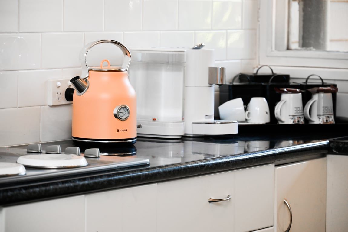A kitchen with a kettle, coffee maker, and a coffee station.