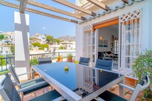 A balcony with a glass table and chairs, potted plants, and a view of the surrounding buildings. - Villa in Nerja Near Burriana Beach (Nerja)