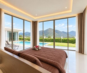 Ein modernes Hotelzimmer mit einem großen Bett, Blick auf einen Swimmingpool und eine Berglandschaft.