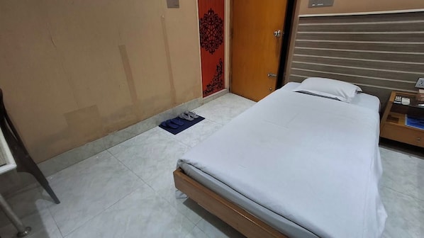 Quarto de hotel com cama, mesa de cabeceira, porta com detalhe decorativo e chão ladrilhado.