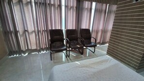 A room with three leather chairs, a bed, and a window with curtains.