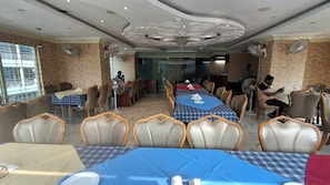 Uma sala de jantar com mesas montadas para vários convidados, cadeiras, ventiladores de teto e um candelabro.