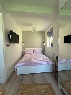 A bedroom with a bed, a television mounted on the wall, a window, and a mirror. - The Little Grove, one bedroom studio; cosy, stylish, peaceful, and central. (Tralee)