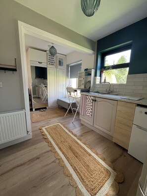 A kitchen with a wooden floor, white cabinets, a window with a view, and a kitchen island. - The Little Grove, one bedroom studio; cosy, stylish, peaceful, and central. (Tralee)