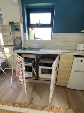A compact kitchen with a built-in oven, a sink, and a window above it. - The Little Grove, one bedroom studio; cosy, stylish, peaceful, and central. (Tralee)