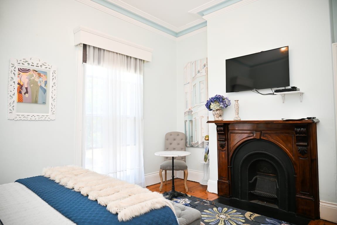 A bedroom with a bed, a television, a fireplace, a small table, and a chair.