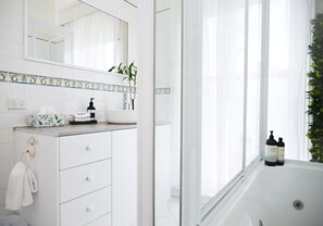 A modern bathroom with a white vanity, a large mirror, and a bathtub. - Deck Quarters-Westwing (Mansfield)