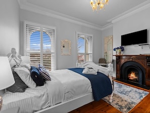 A bedroom with a bed, a fireplace, a television, and a window with shutters. - Deck Quarters-Westwing (Mansfield)
