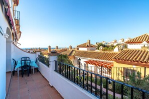 A balcony with a table and chairs, overlooking a coastal town with terracotta-roofed buildings. - Apartment in Nerja Near Burriana Beach (Nerja)
