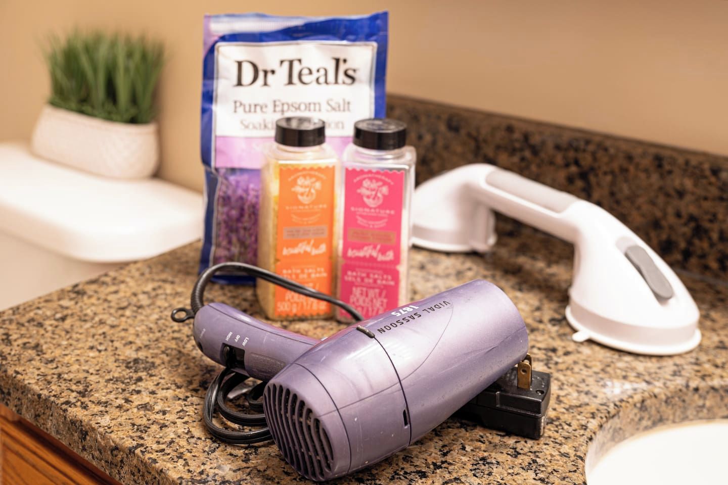 A hairdryer, a package of Dr. Teal's Pure Epsom Salt, and a white telephone on a granite countertop.