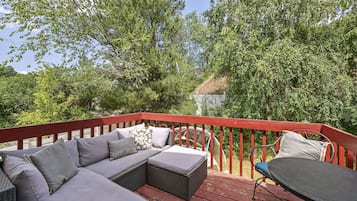 Een terras met een rode balustrade, een grijze bank met decoratieve kussens en een ronde tafel.