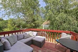 Een terras met een rode balustrade, een grijze bank met decoratieve kussens en een ronde tafel.