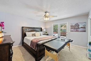 Une chambre à coucher comprenant un lit, un bureau, un ventilateur de plafond et une porte donnant sur un espace extérieur.