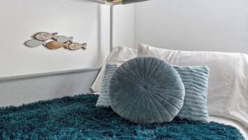 A bed with a teal furry rug, two pillows, and a wall with a wooden shelf holding decorative fish.