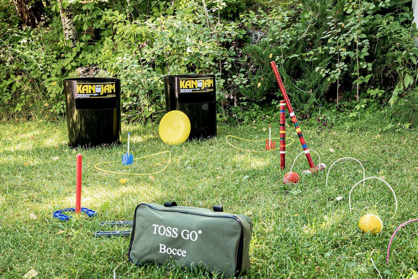 Ein grünes Freigelände mit einer TOSS GO Bocce-Tasche, zwei schwarzen Mülleimern, einem gelben Frisbee und einem Satz farbiger Bocce-Stäbe.