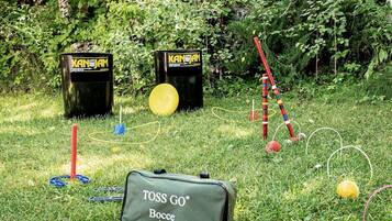 Ein grünes Freigelände mit einer TOSS GO Bocce-Tasche, zwei schwarzen Mülleimern, einem gelben Frisbee und einem Satz farbiger Bocce-Stäbe.