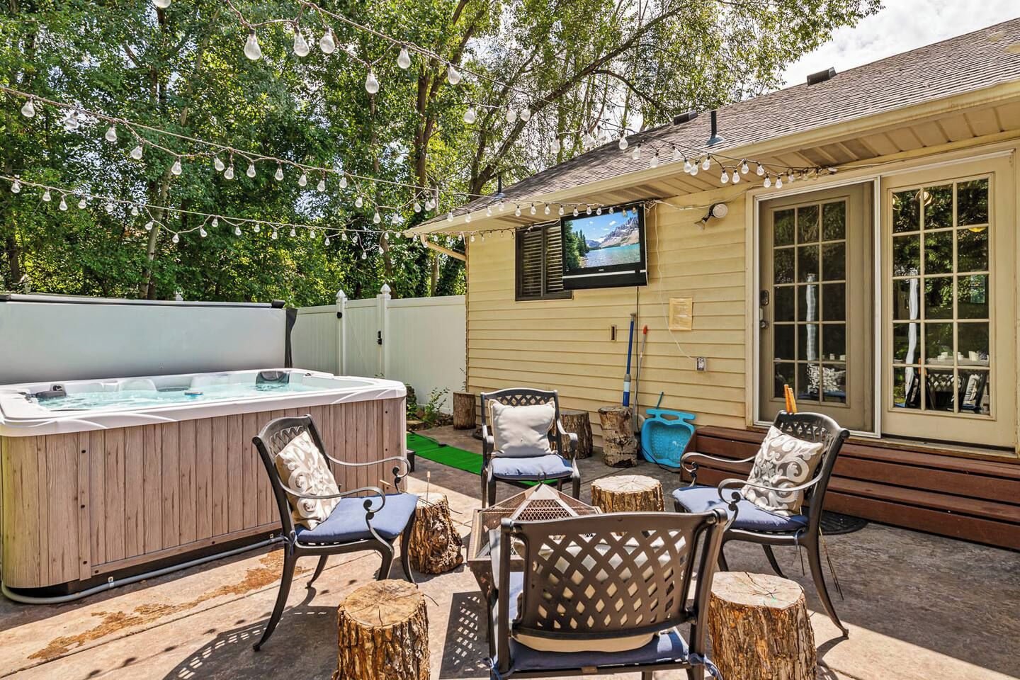 An outdoor patio with a hot tub, chairs, and a TV mounted on the wall.