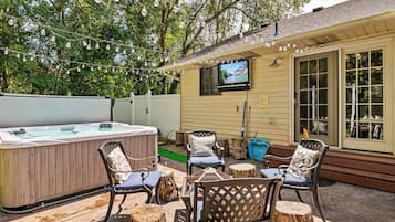 An outdoor patio with a hot tub, chairs, and a TV mounted on the wall.