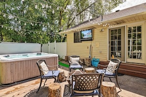 An outdoor patio with a hot tub, chairs, and a TV mounted on the wall.