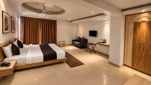 A modern hotel room with a bed, bedside table, a flat-screen TV, a wardrobe, and a small seating area with a sofa and a coffee table.