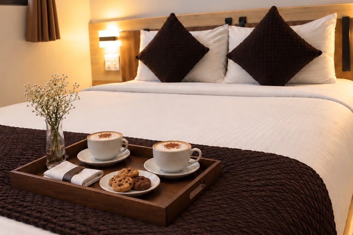A hotel room with a bed, a tray with coffee and cookies, a vase with flowers, and a wall art piece.